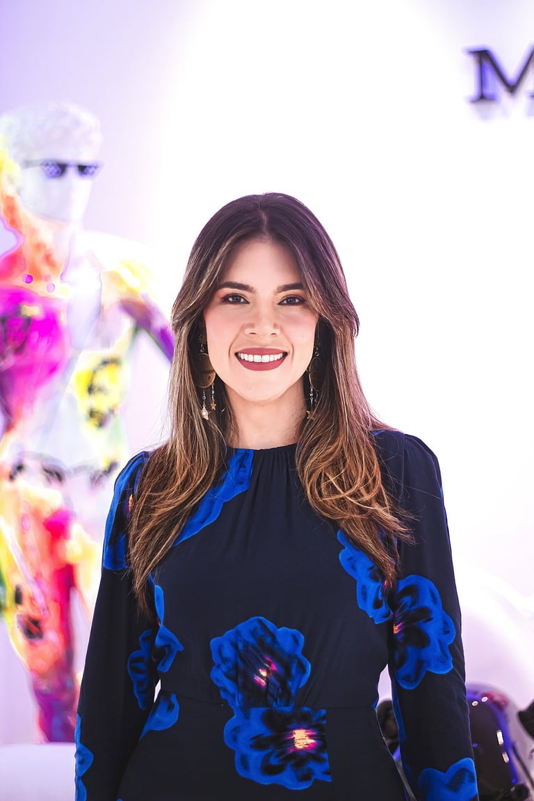 Natalia Devia sonriendo, con vestido azul de flores, frente a arte colorido